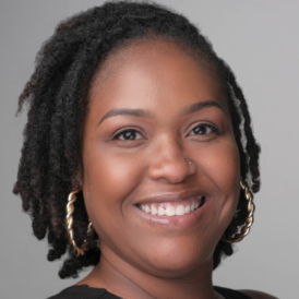 headshot of Black woman with shoulder length locs wearing hoop earrings smiling into the camera
