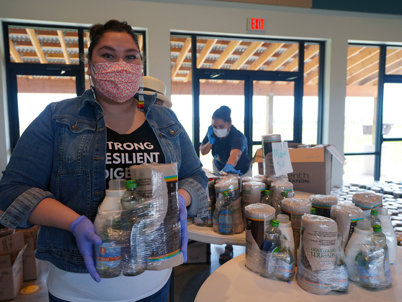 Woman holding a wrapped package of paper towels and other cleaning products to give away.
